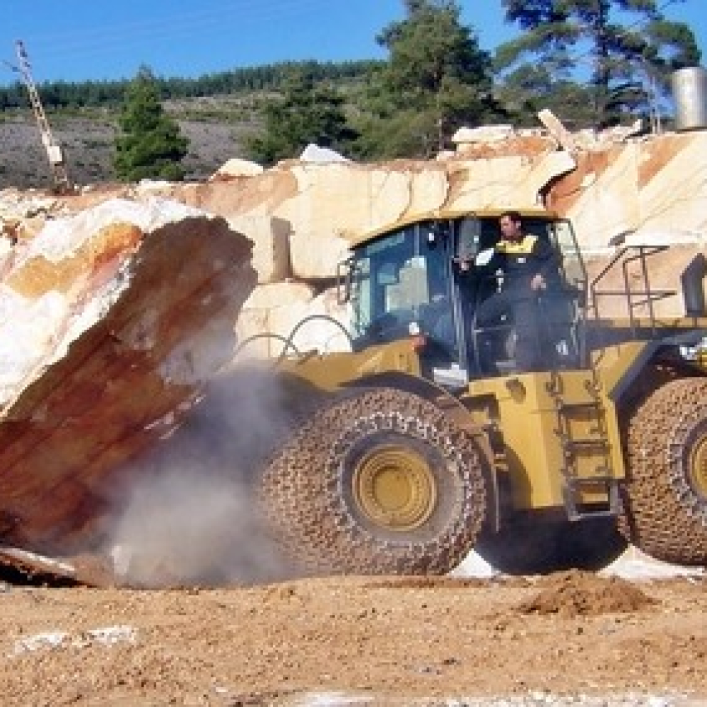 Heavy machinery operating in a quarry, moving a large rock boulder.