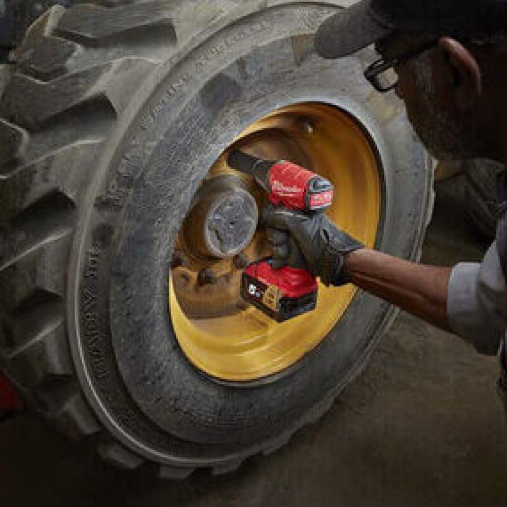 A worker uses a power tool on a construction vehicle's large tire.