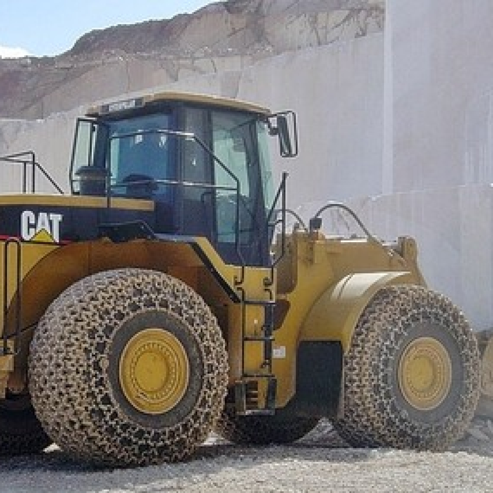 Heavy machinery loader with tire protection chains on a quarry site.