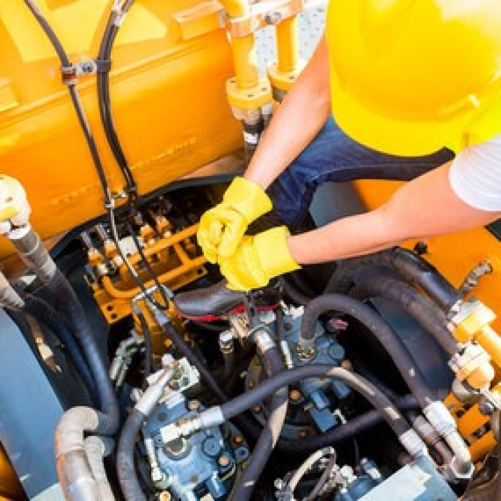 Worker inspecting the hydraulic system in a heavy machinery operation.
