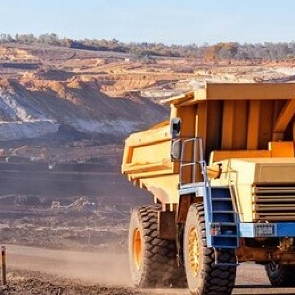 Heavy dump truck driving at a mining site with large excavation area.