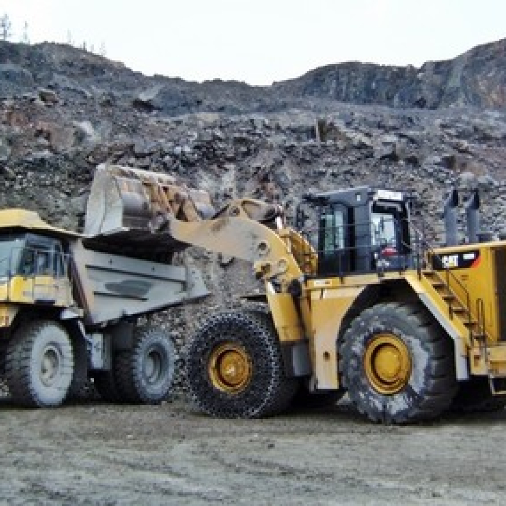 Heavy machinery in operation at a mining site with traction chains visible.