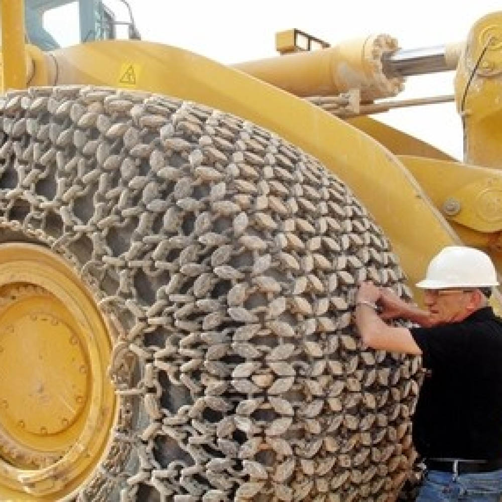 A worker adjusts a tire protection chain on heavy machinery's large tire.