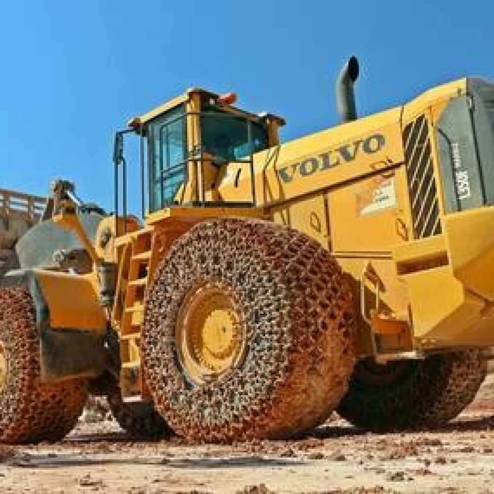 Wheel loader equipped with traction chains, operating in a construction site setting.